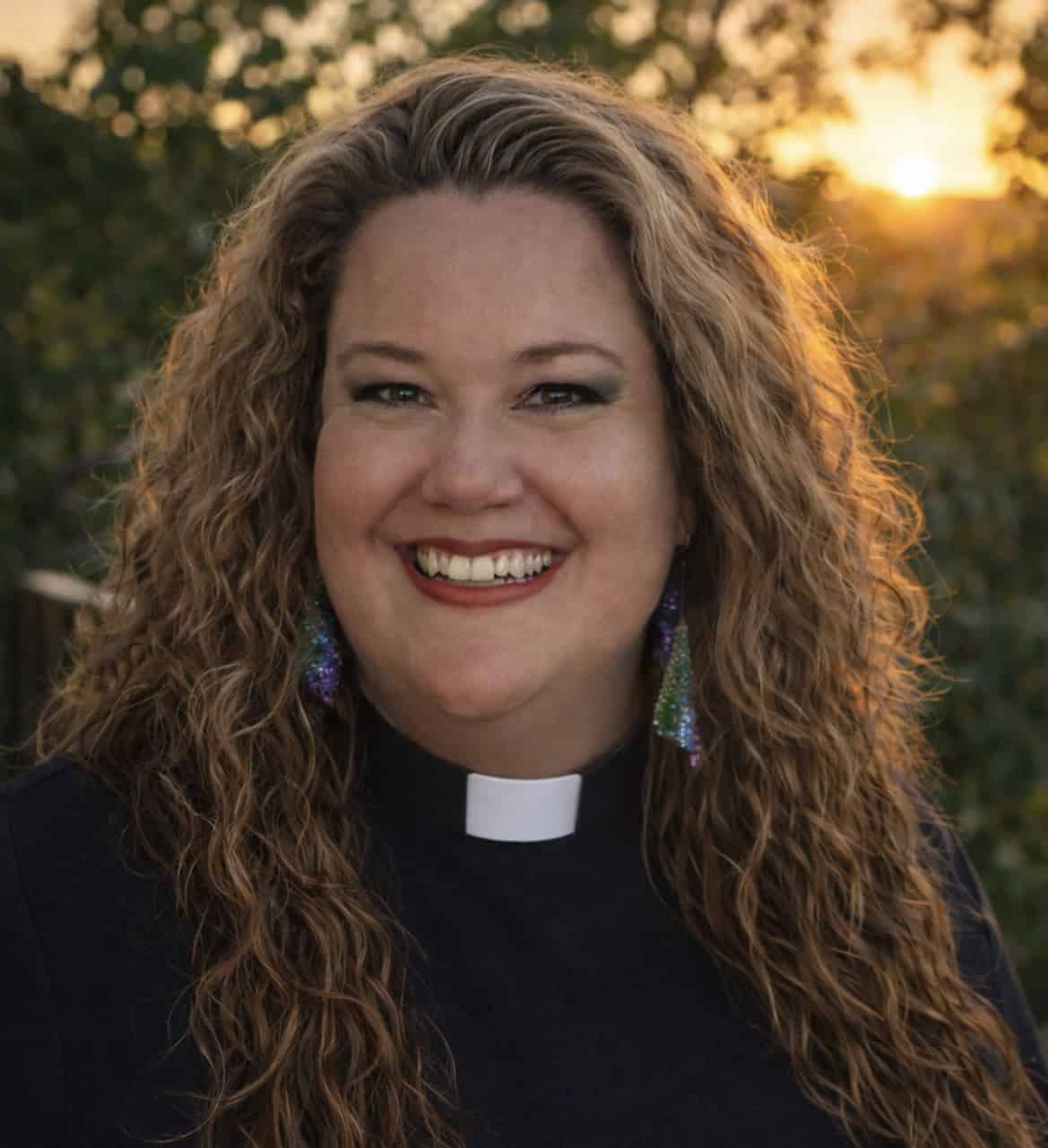 Bright smiling woman in clergy attire outdoors during sunset, promoting More Light Presbyterians.
