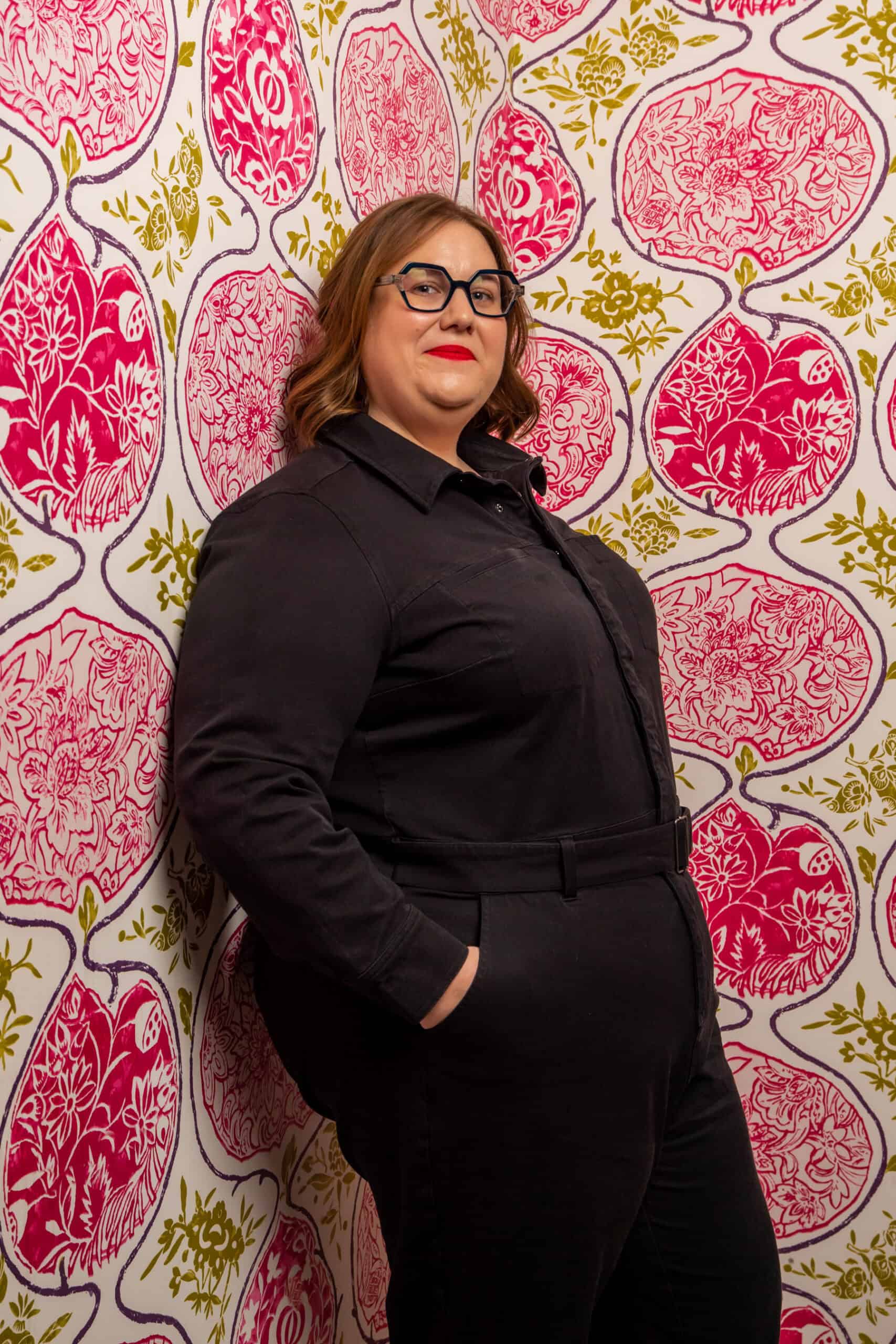 Sarah leer Empowered woman standing confidently against vibrant pink and gold patterned wallpaper.